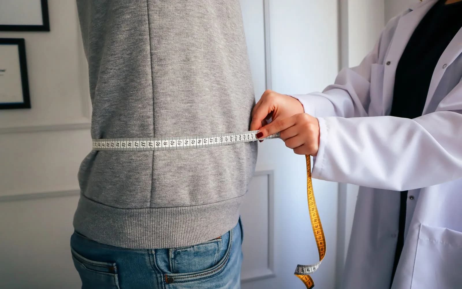 A clinician's hands holding a tape measure around a man's waist over a grey sweatshirt