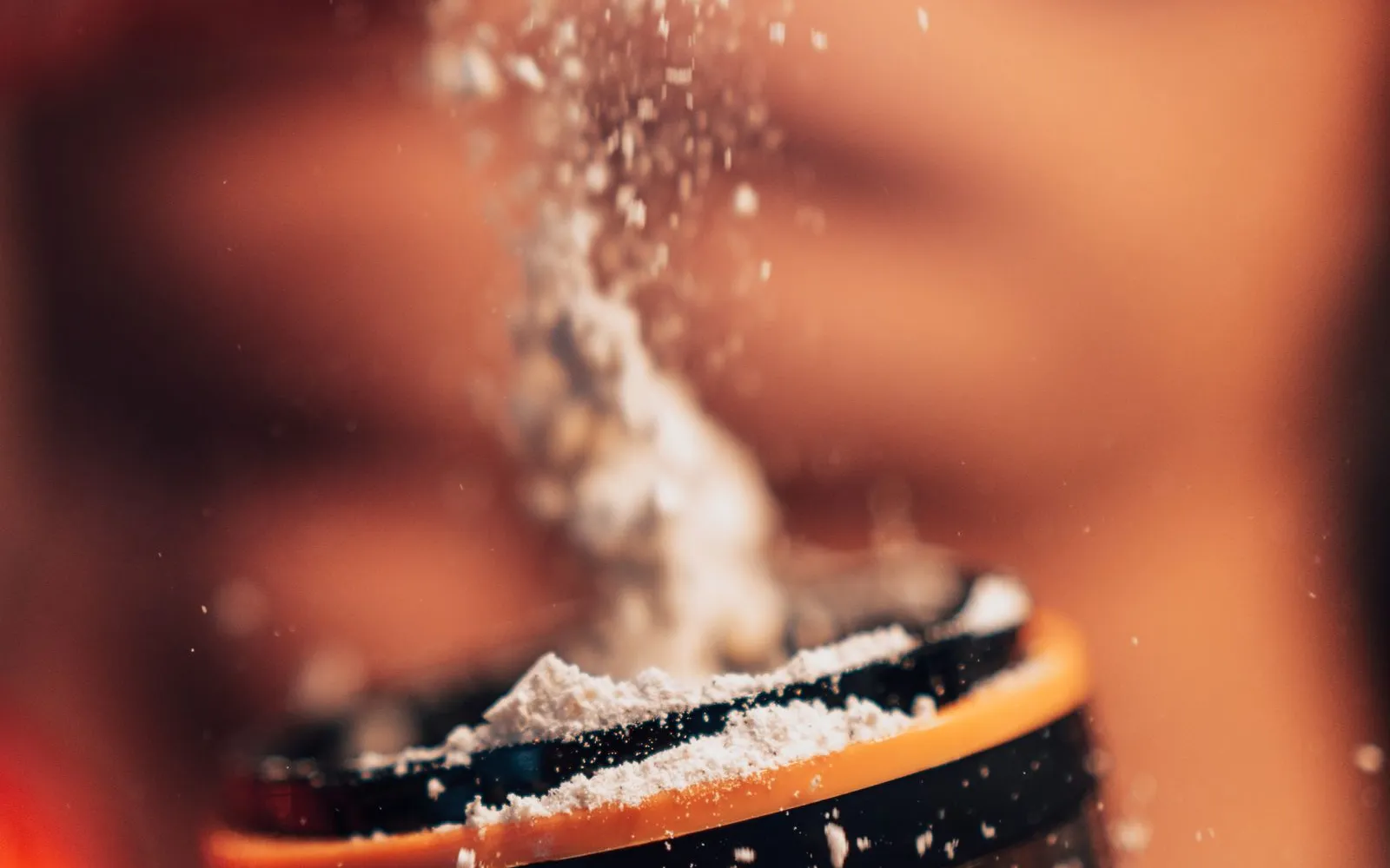 White powder pouring from a scoop into a shaker bottle.