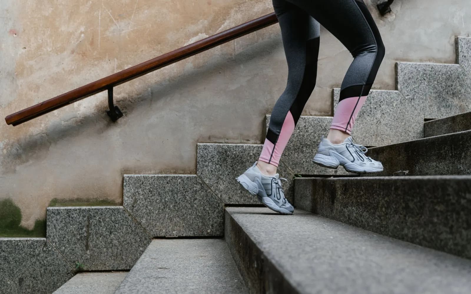 Legs in leggings and grey trainers running up outdoor stone steps beside a handrail.