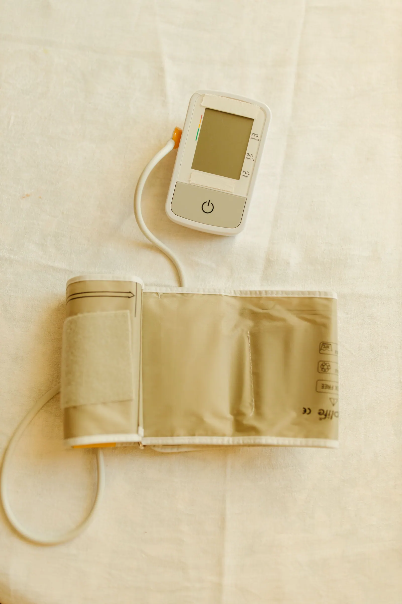 A digital blood pressure monitor and upper-arm cuff on white fabric.