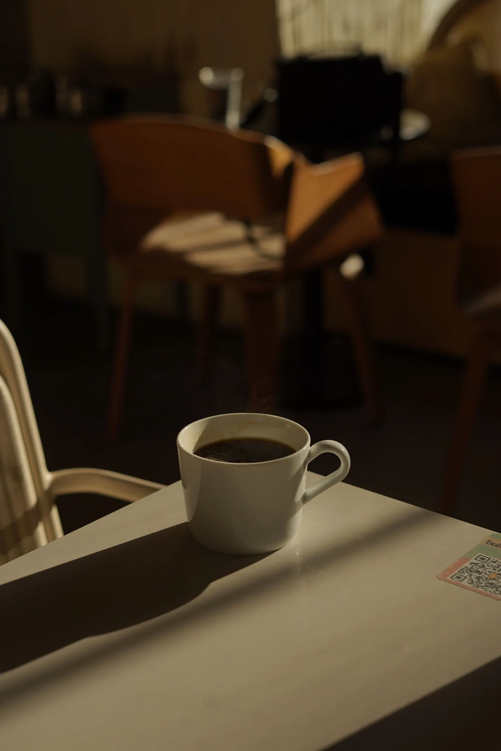 A cup of coffee on a table in sunlight.