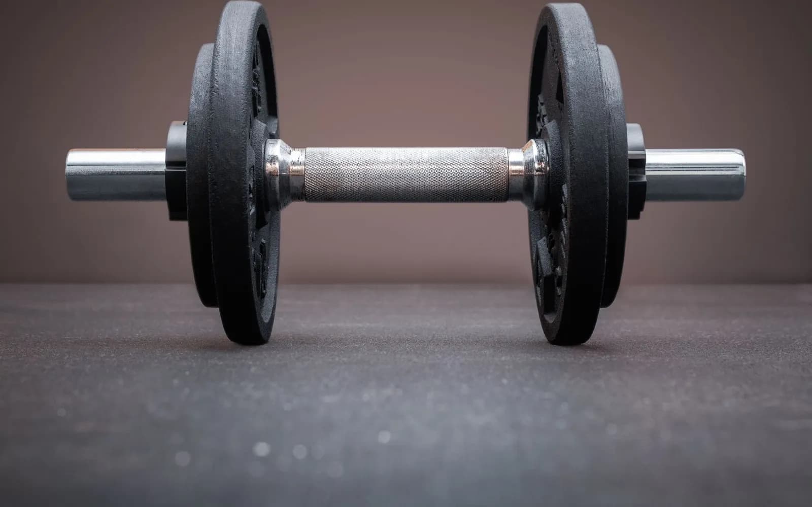 A dumbbell loaded with black iron plates resting on a dark gym floor