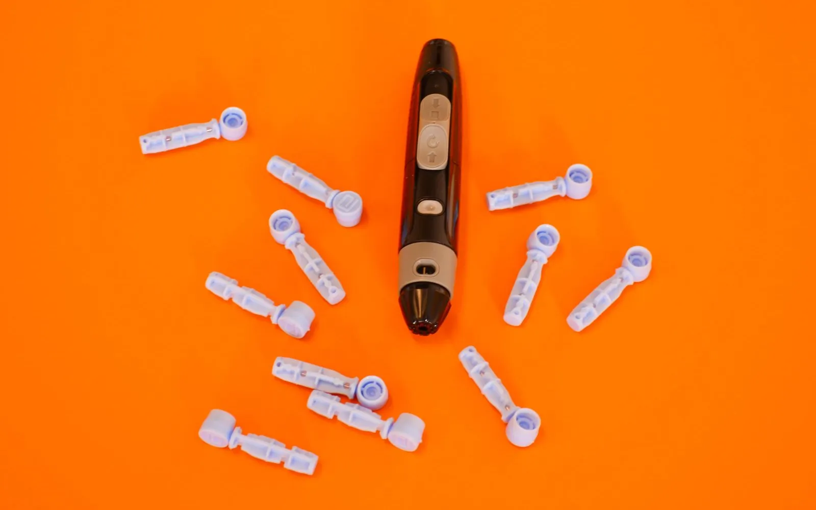 A finger-prick lancing pen surrounded by spare lancets on an orange background