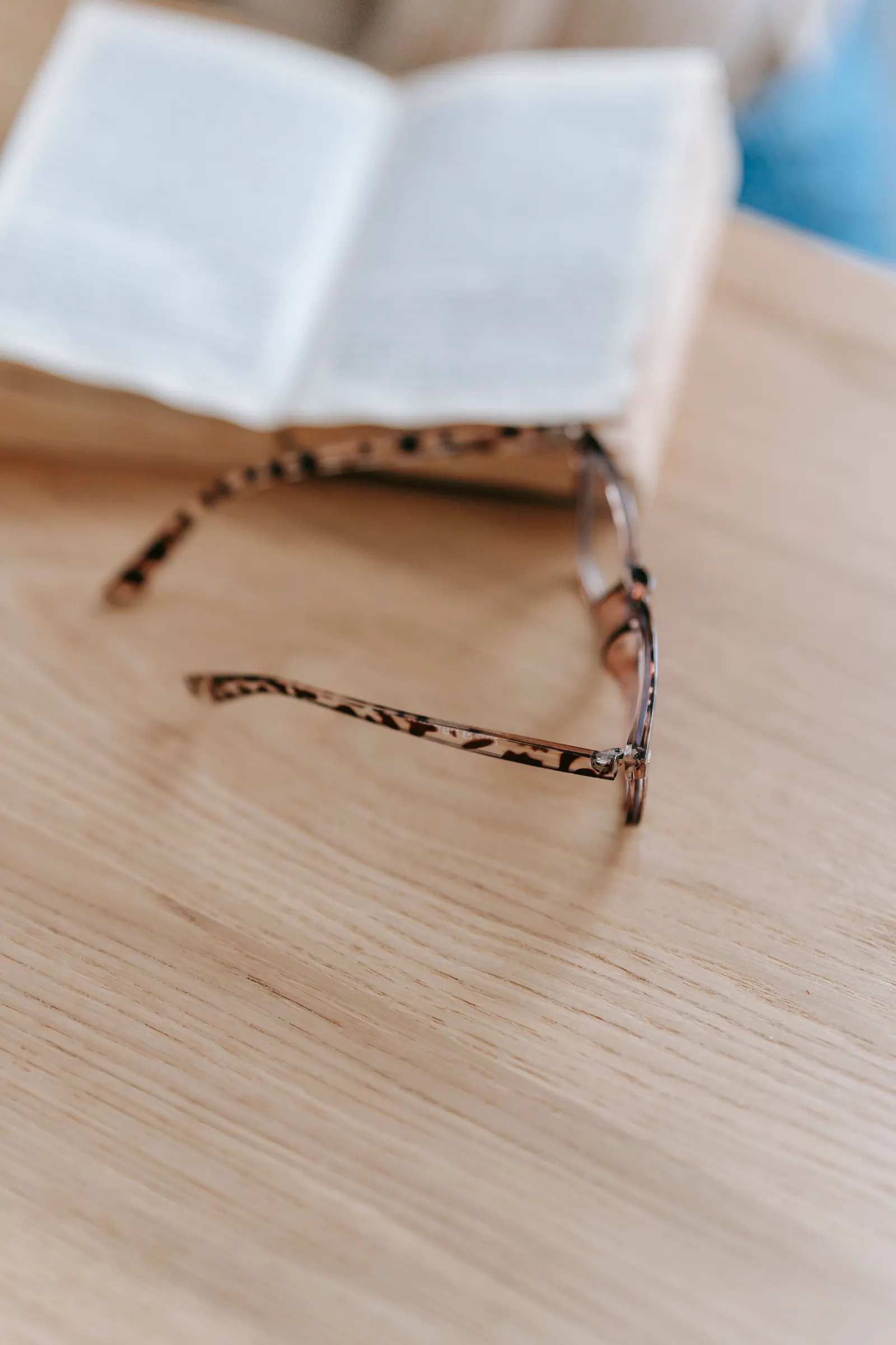 Reading glasses beside an open book on a wooden table.