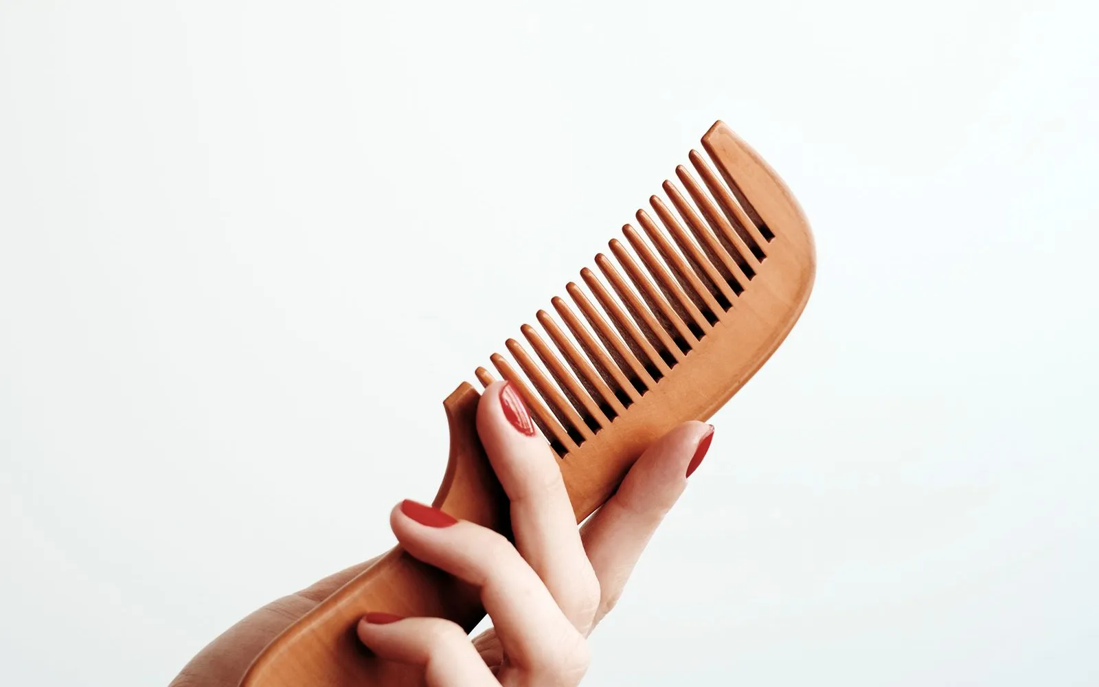 A hand holding a wooden comb against a plain white background