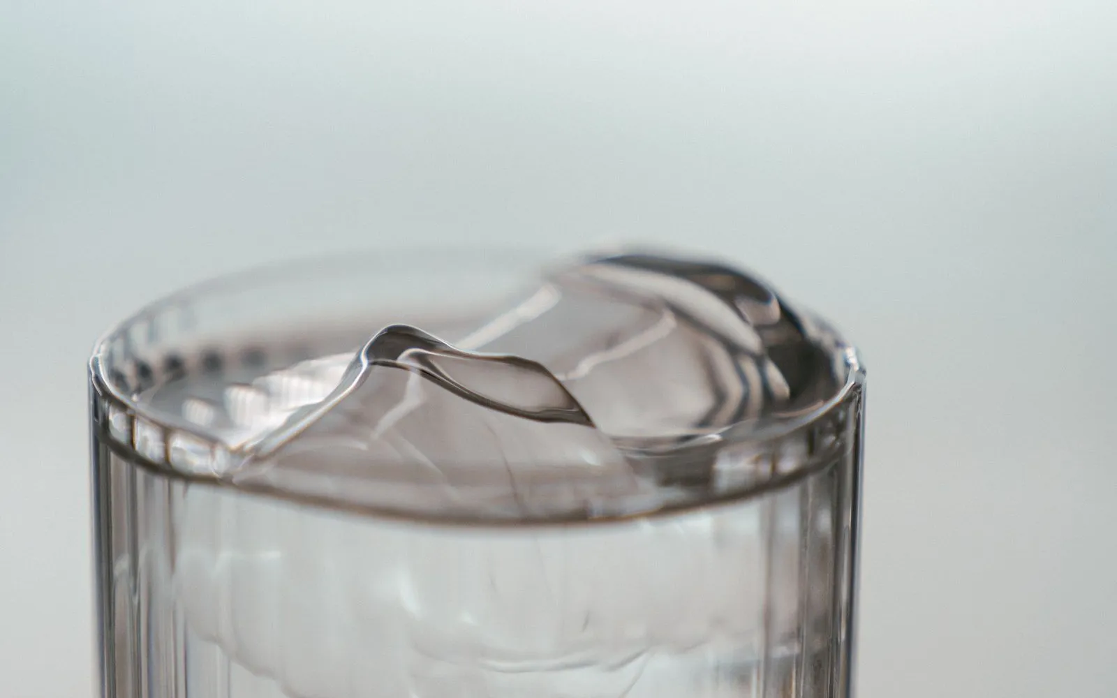 A tall clear glass of water with ice cubes against a pale background.
