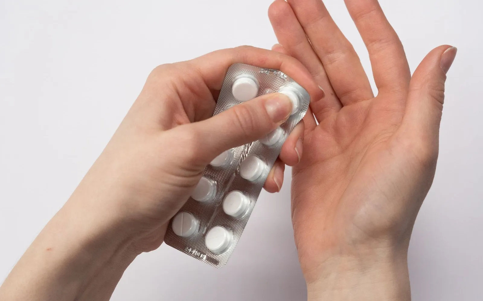 Hands pressing a white tablet out of a silver blister pack into an open palm
