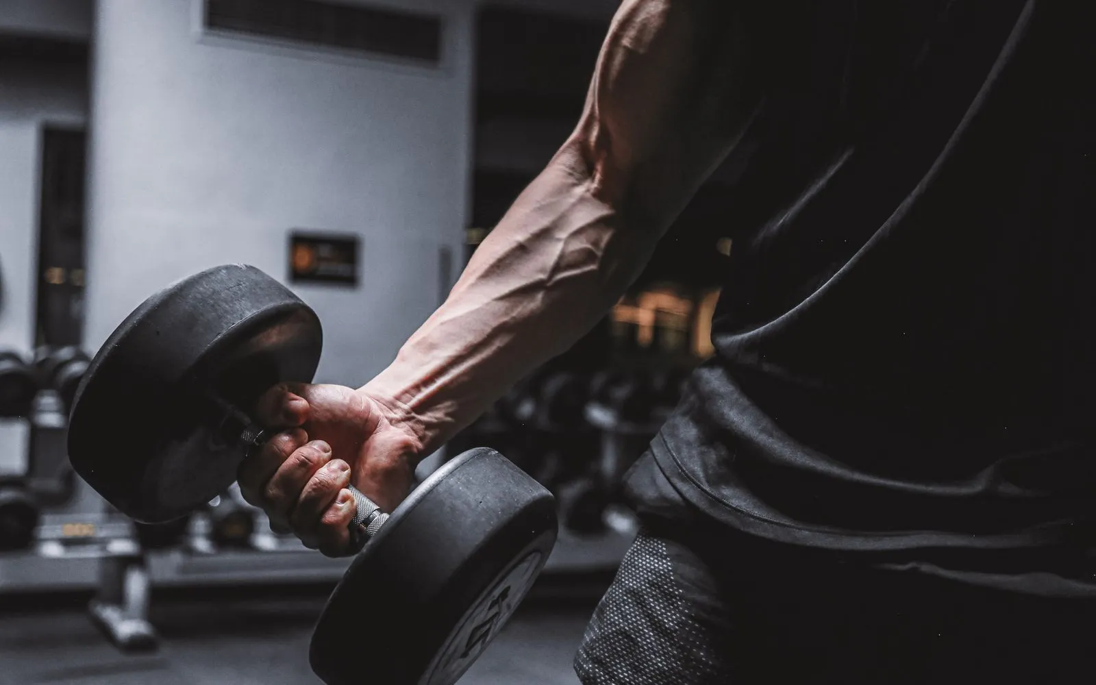 A forearm and hand gripping a dumbbell in a gym, face out of frame