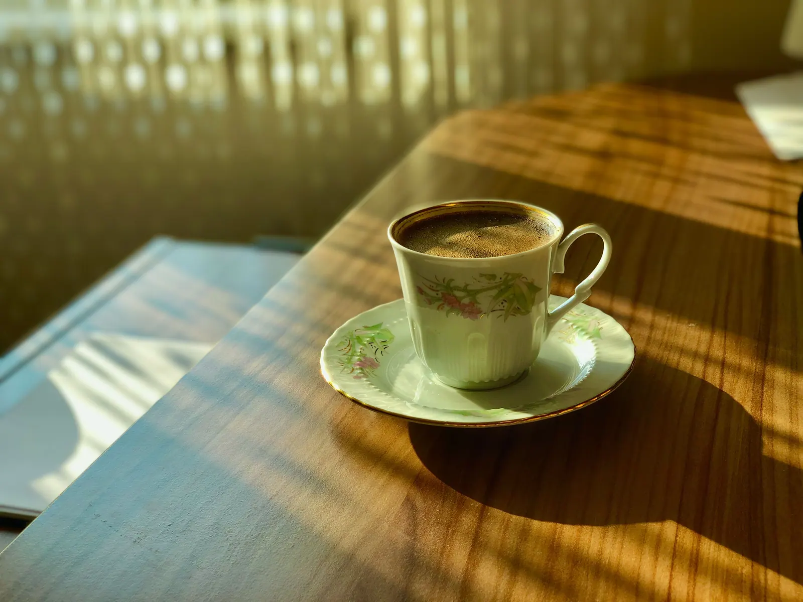 A small coffee cup catching morning light on a wooden table.