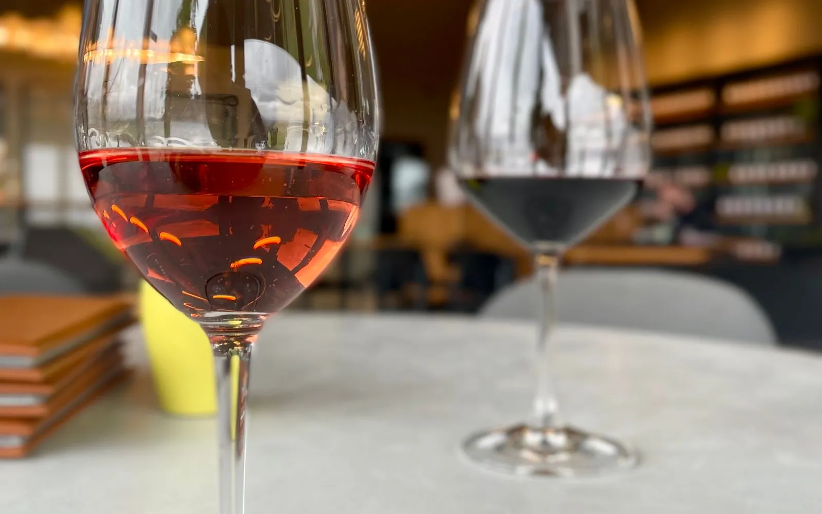 A glass of rosé and a glass of red on a pale table, with a blurred café behind