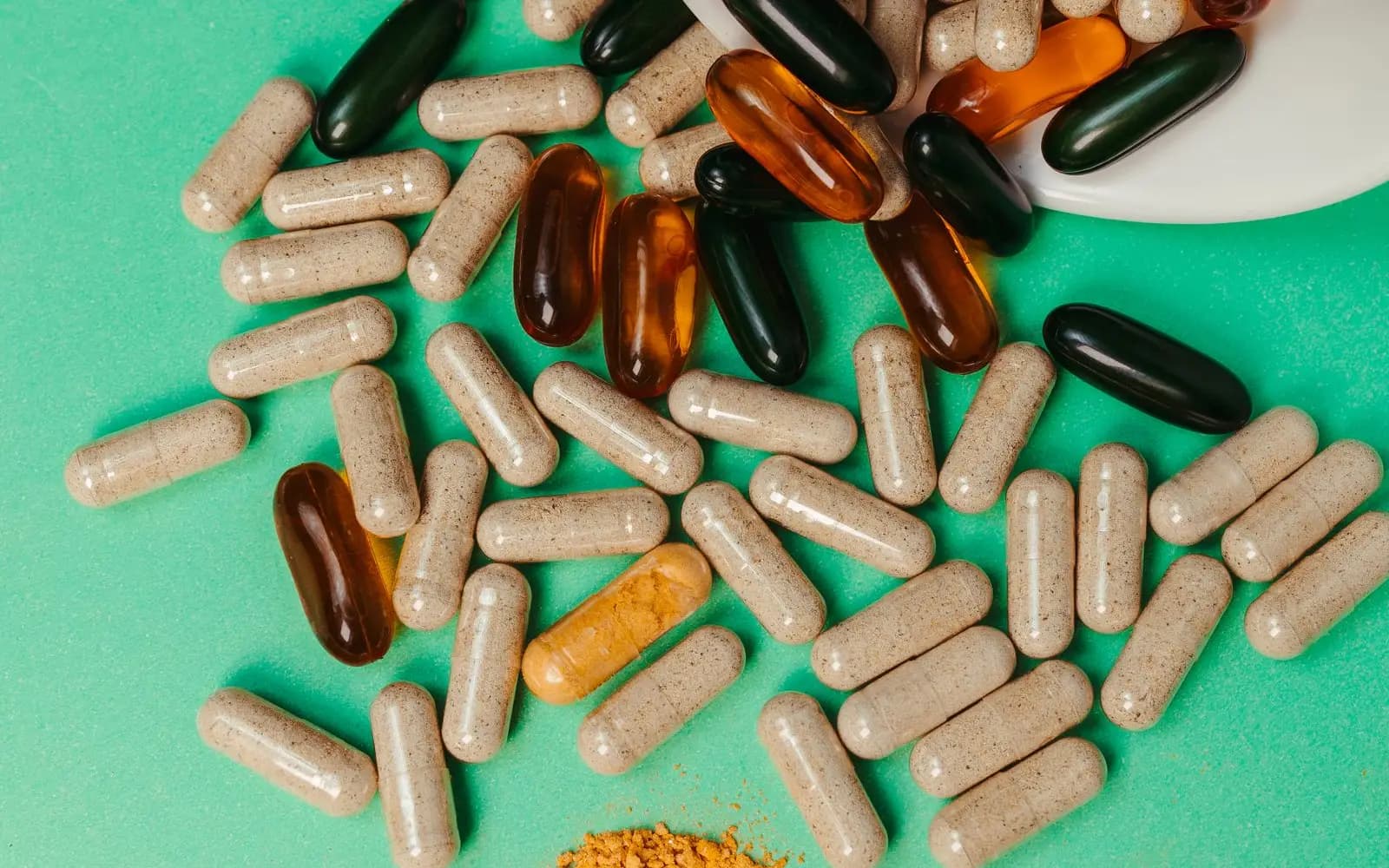 Supplement capsules spilling from a white dish onto a green surface.