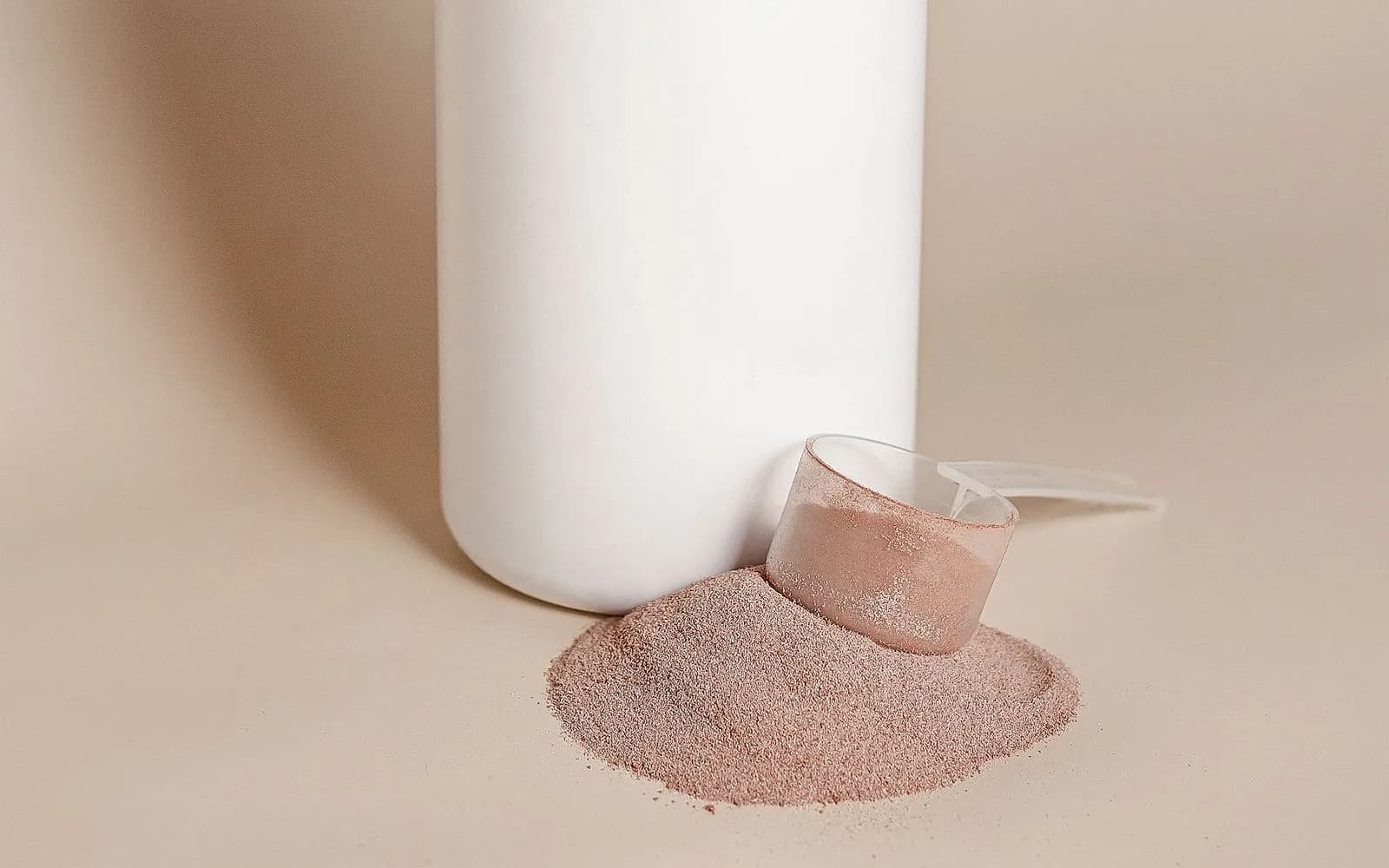 A plain white tub with a clear scoop resting in a small pile of light brown powder.