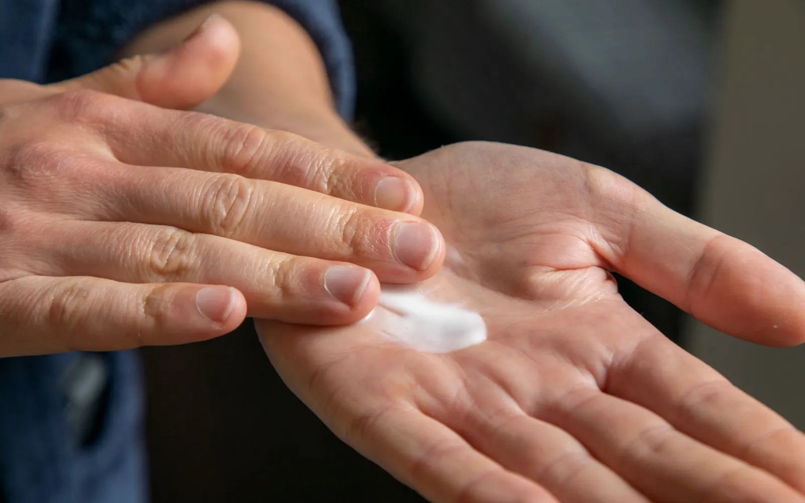 Two hands, one with a dab of white cream in the palm, the other's fingertips about to spread it