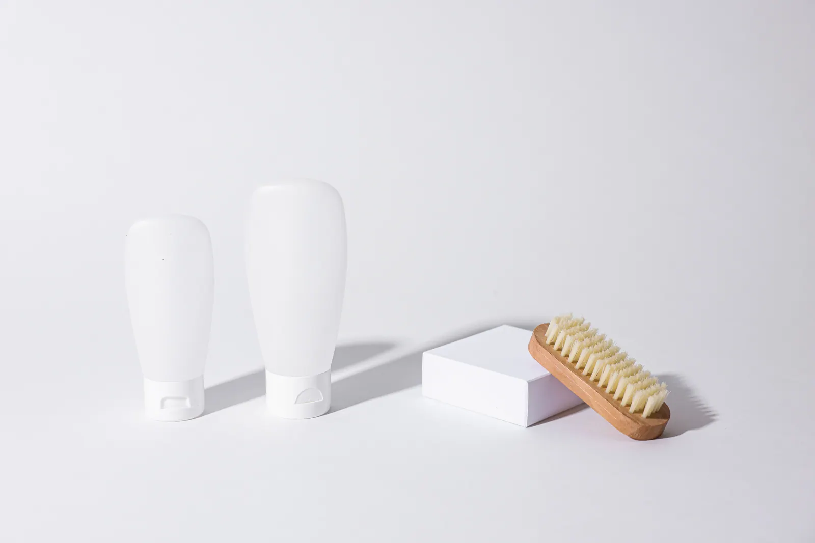 Plain skincare containers and a wooden brush on a light background.