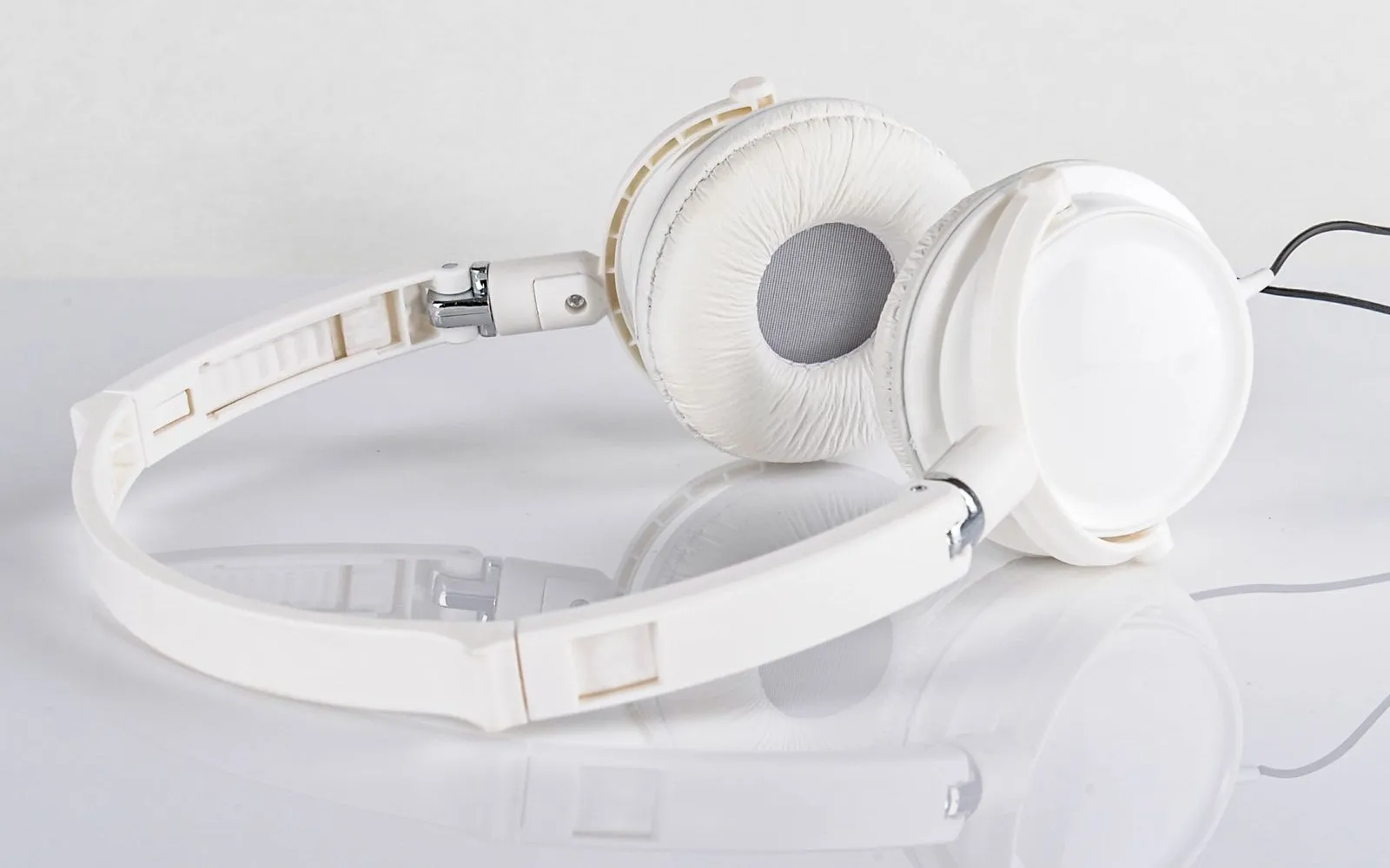 White wired headphones resting on a pale reflective surface.