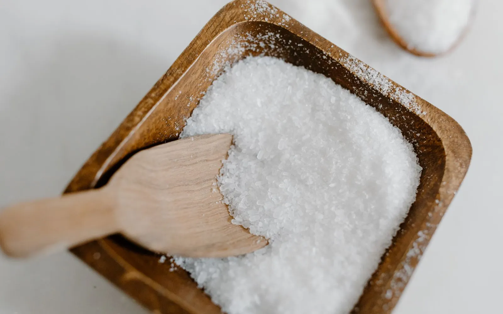 Coarse white salt in a square wooden bowl with a small wooden scoop