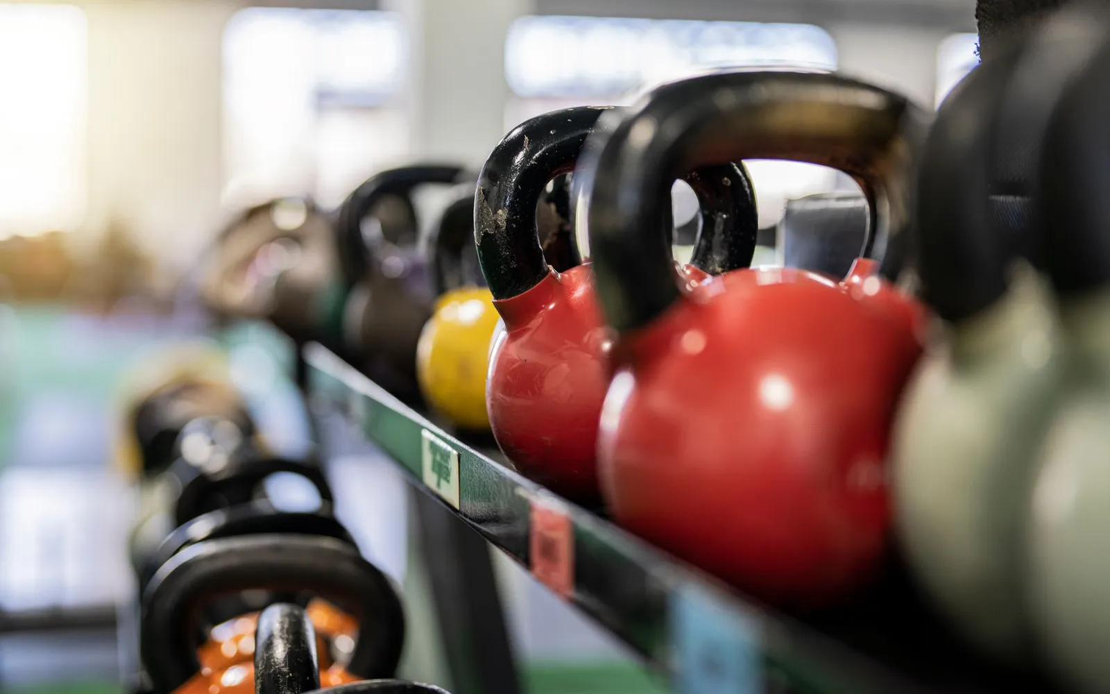 Rows of kettlebells on a gym rack, with red ones in focus.