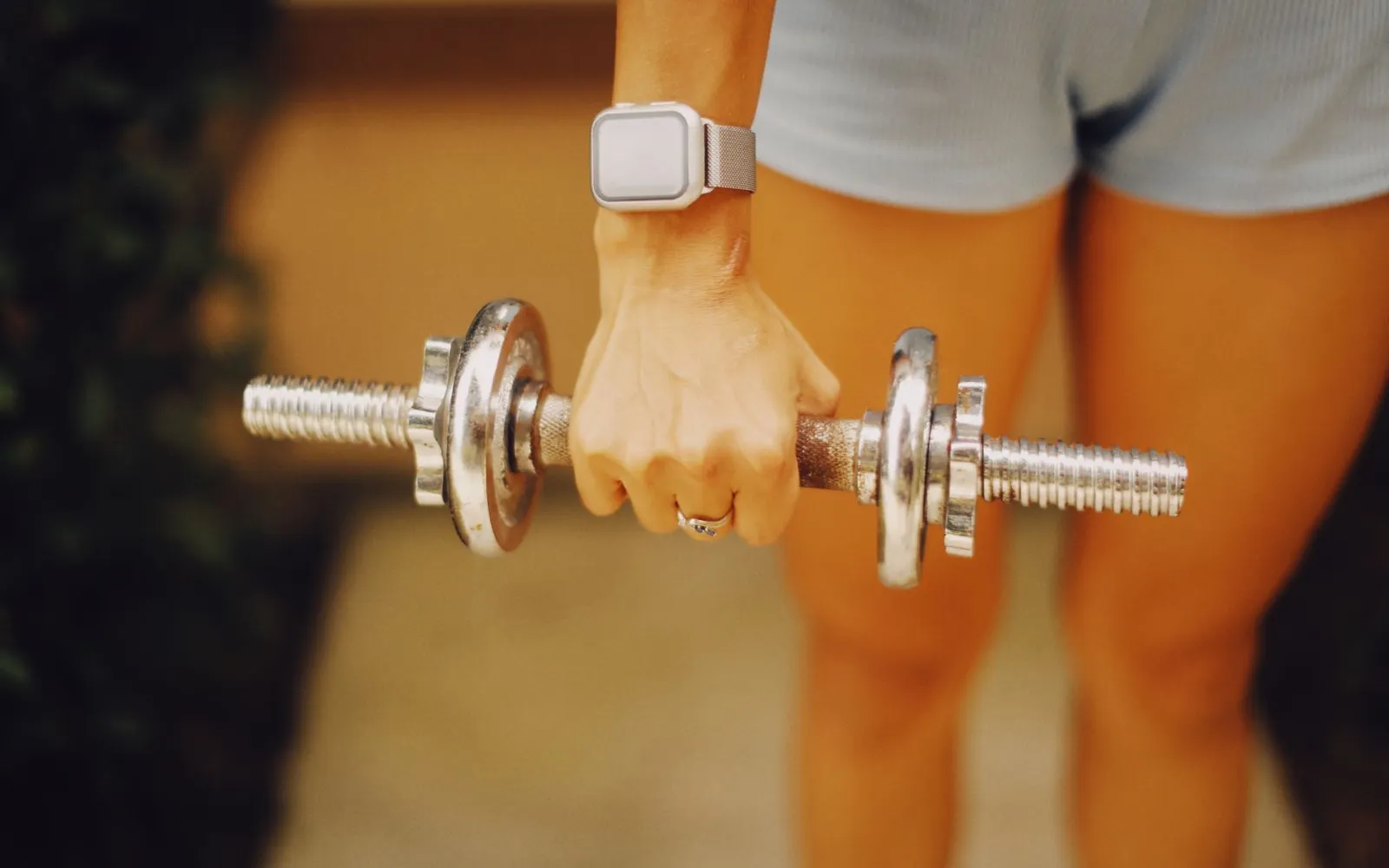 A woman's hand gripping a small metal dumbbell at her side, face not shown