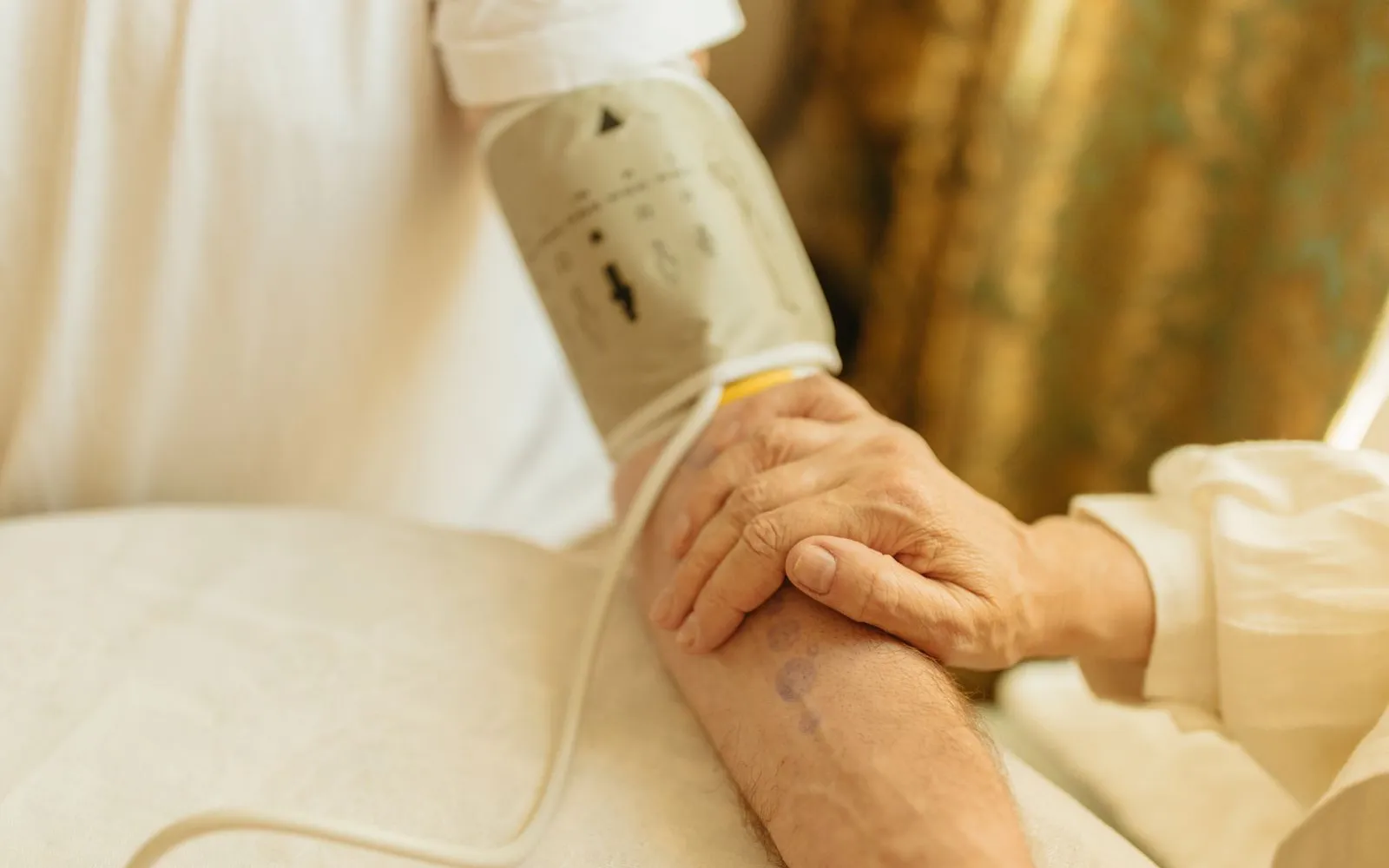 A hand resting on someone's forearm while a blood pressure cuff is fitted to their upper arm at a table