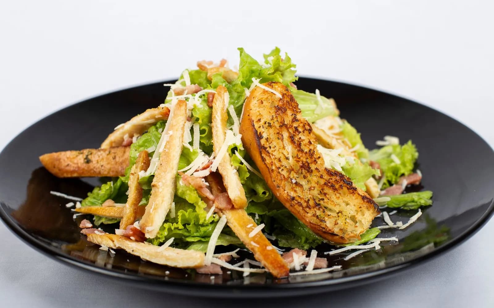 A chicken salad with croutons, grated cheese and bacon bits on a black plate