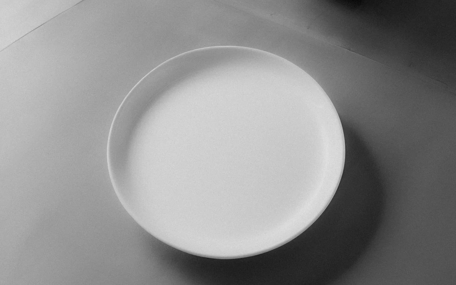 An empty white plate on a plain table, in black and white
