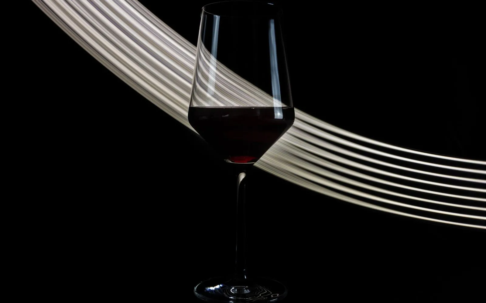 A glass of red wine on a black background with a curved streak of light behind it