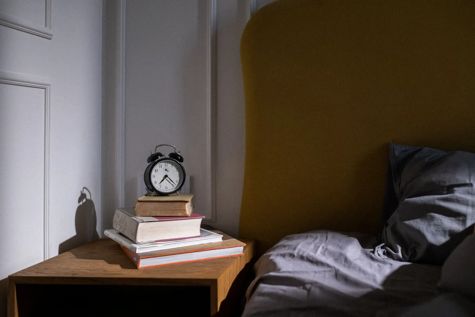 Books and an alarm clock beside a bed.