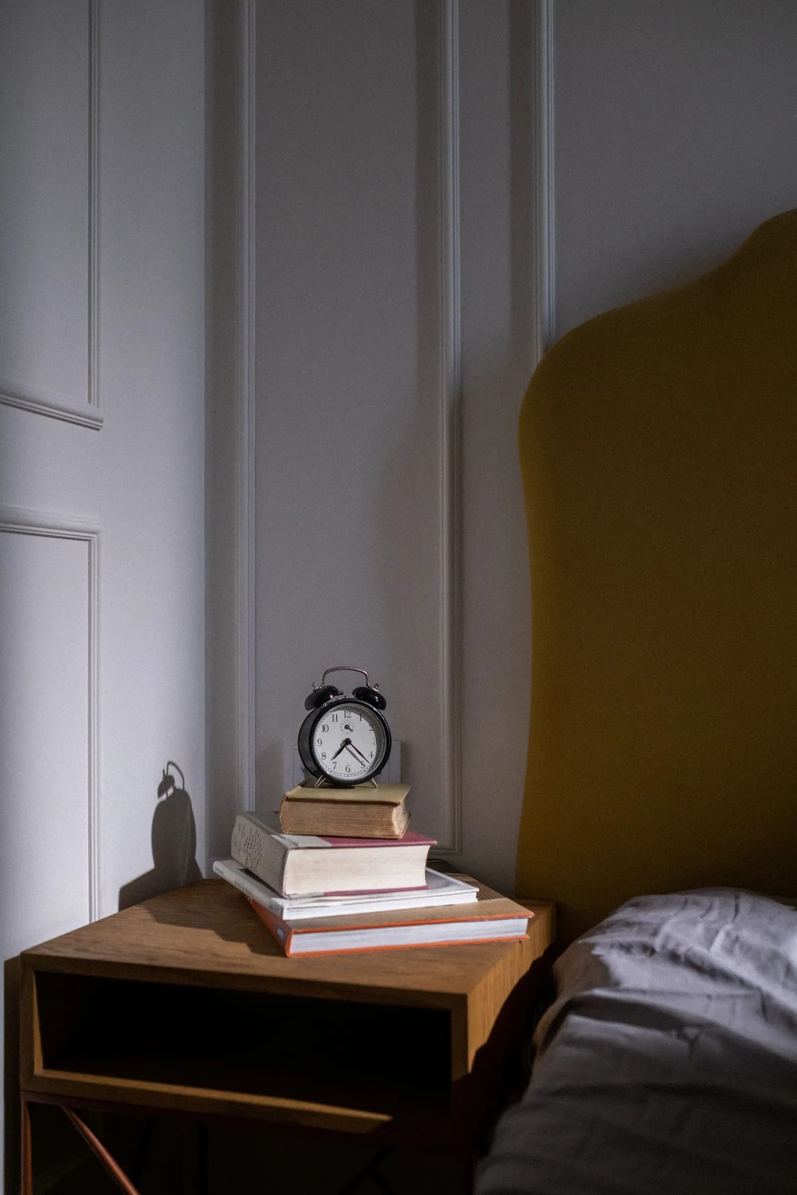 A bedside clock and a stack of books in a quiet bedroom.