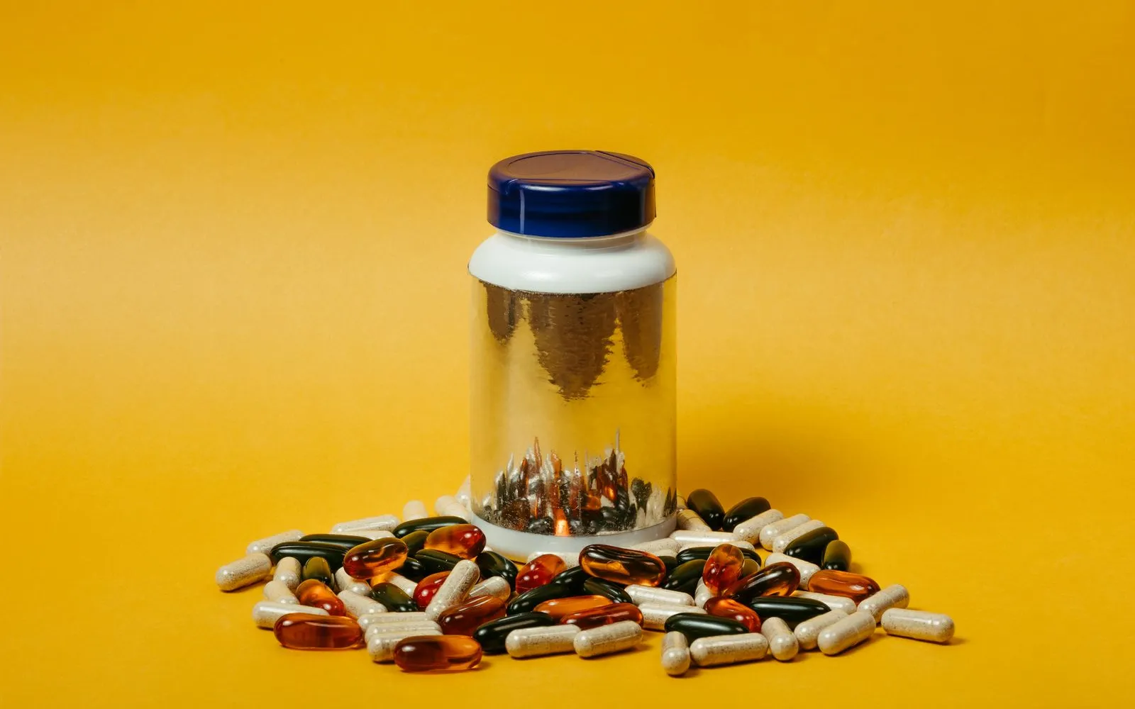 A plain supplement tub surrounded by capsules and fish oil softgels on a yellow background
