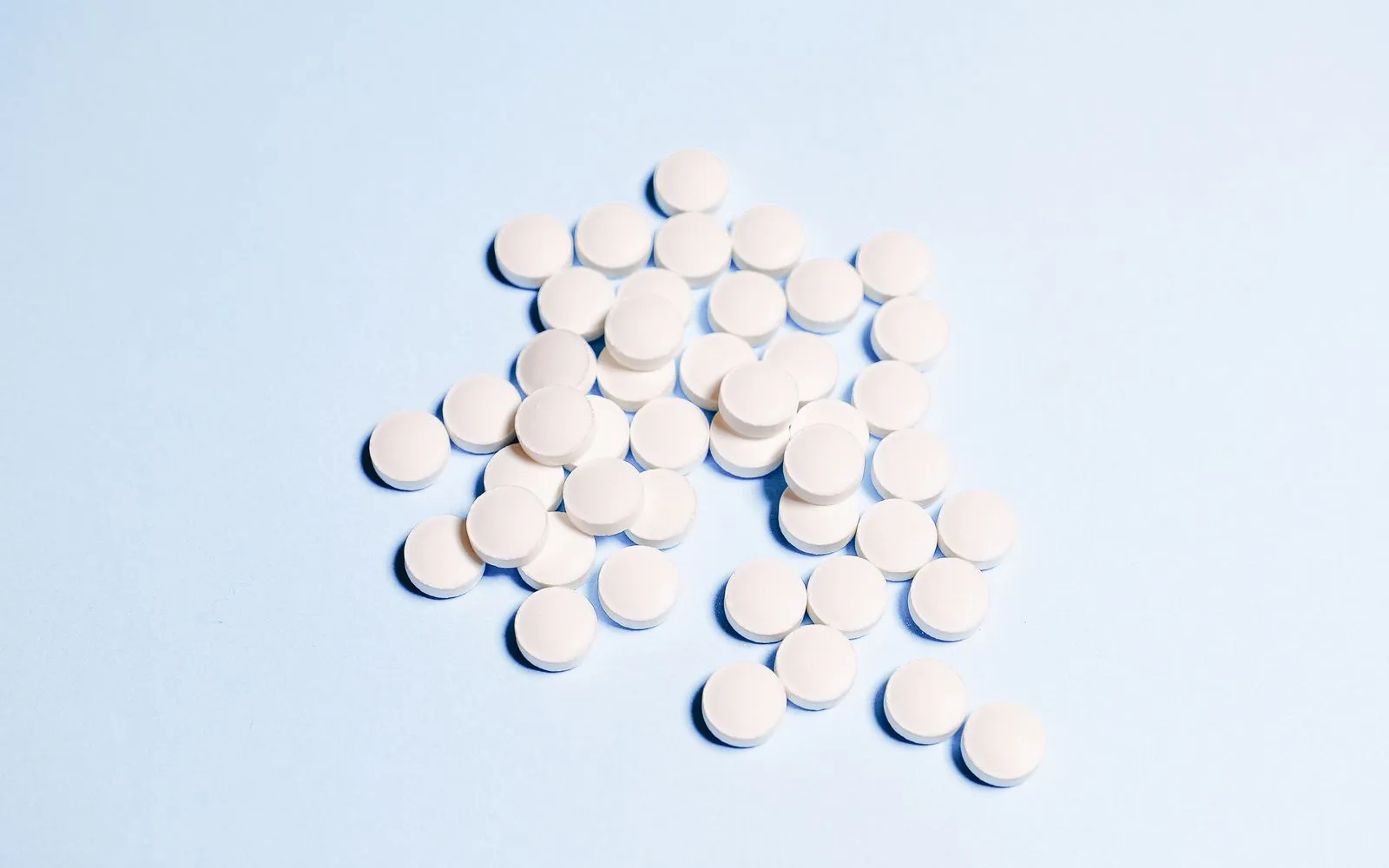 A small pile of plain white round tablets on a pale blue surface