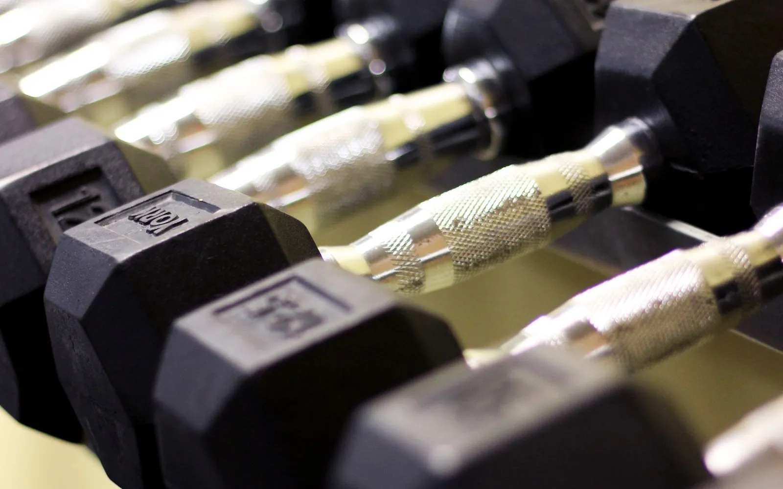 A row of black hexagonal dumbbells with knurled metal handles on a gym rack.