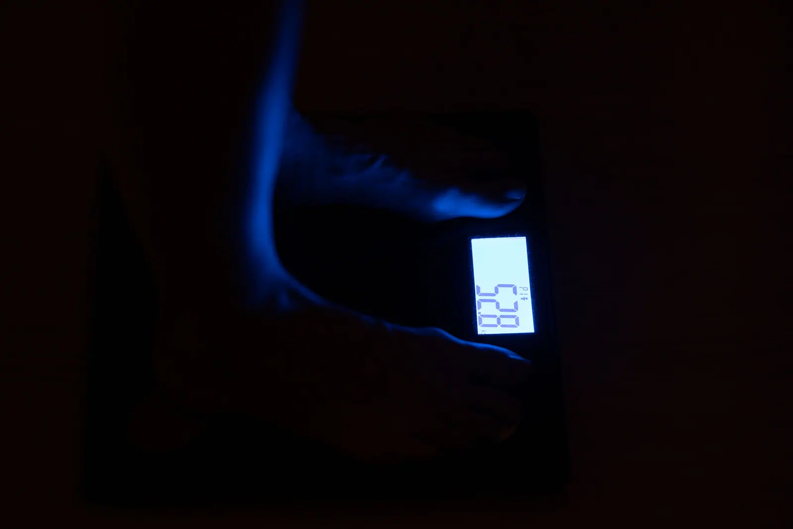 Feet on a digital bathroom scale, with its display illuminated.