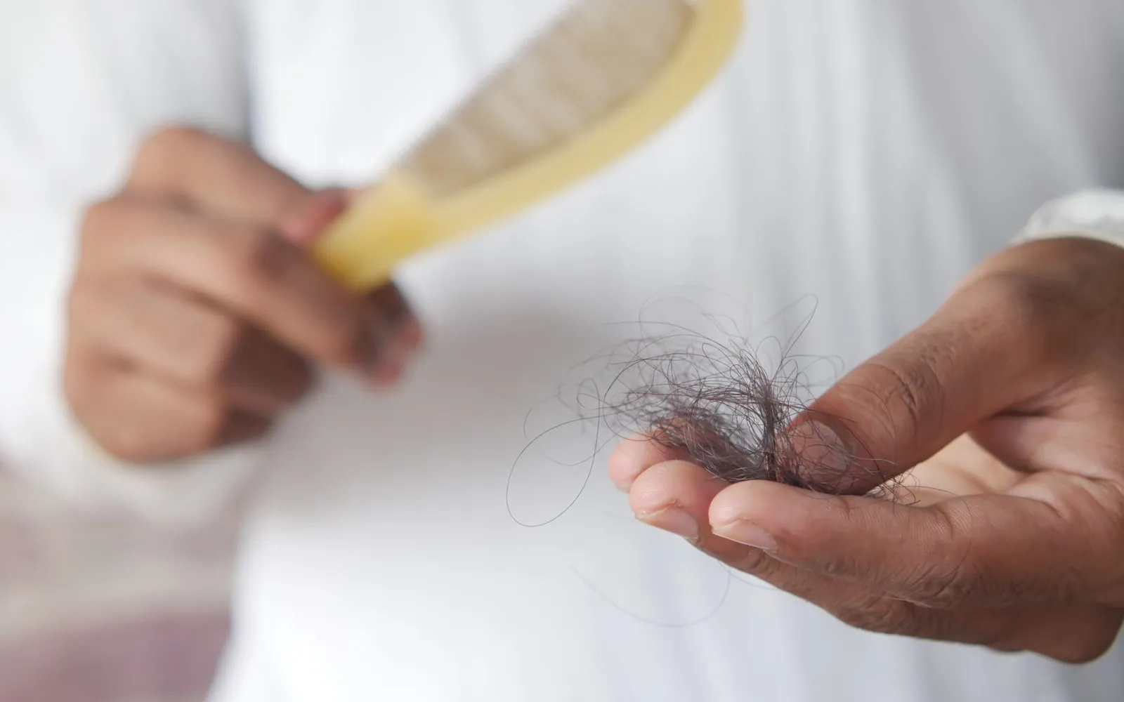 One hand holds a small clump of shed dark hair while the other holds a plastic comb
