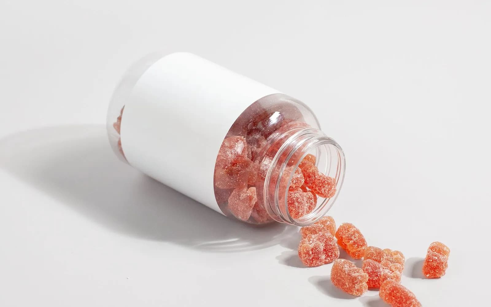Orange gummy vitamins spilling from a tipped-over jar with a blank label on a white surface