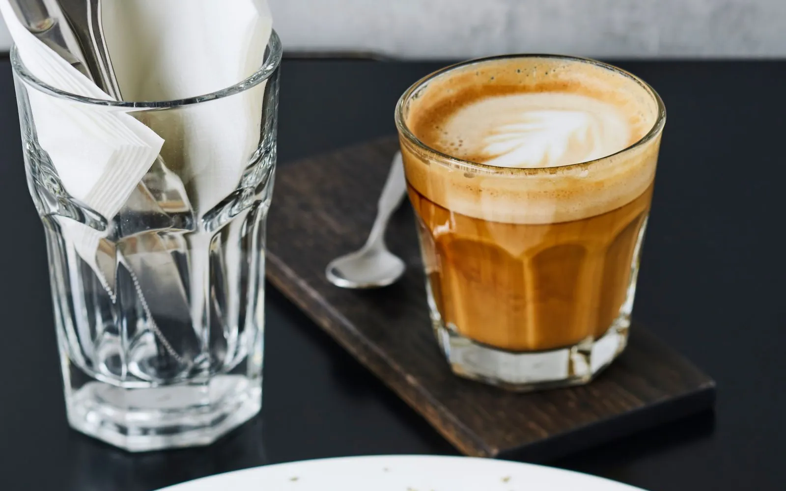 A plate of poached eggs on toast with a glass of milky coffee behind it on a dark table