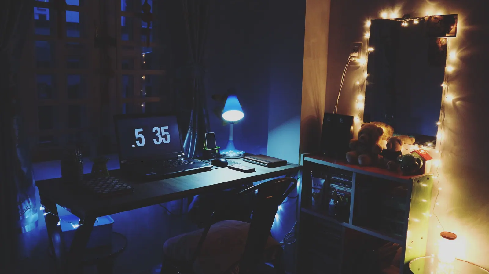A laptop and clock on a desk lit for evening work.