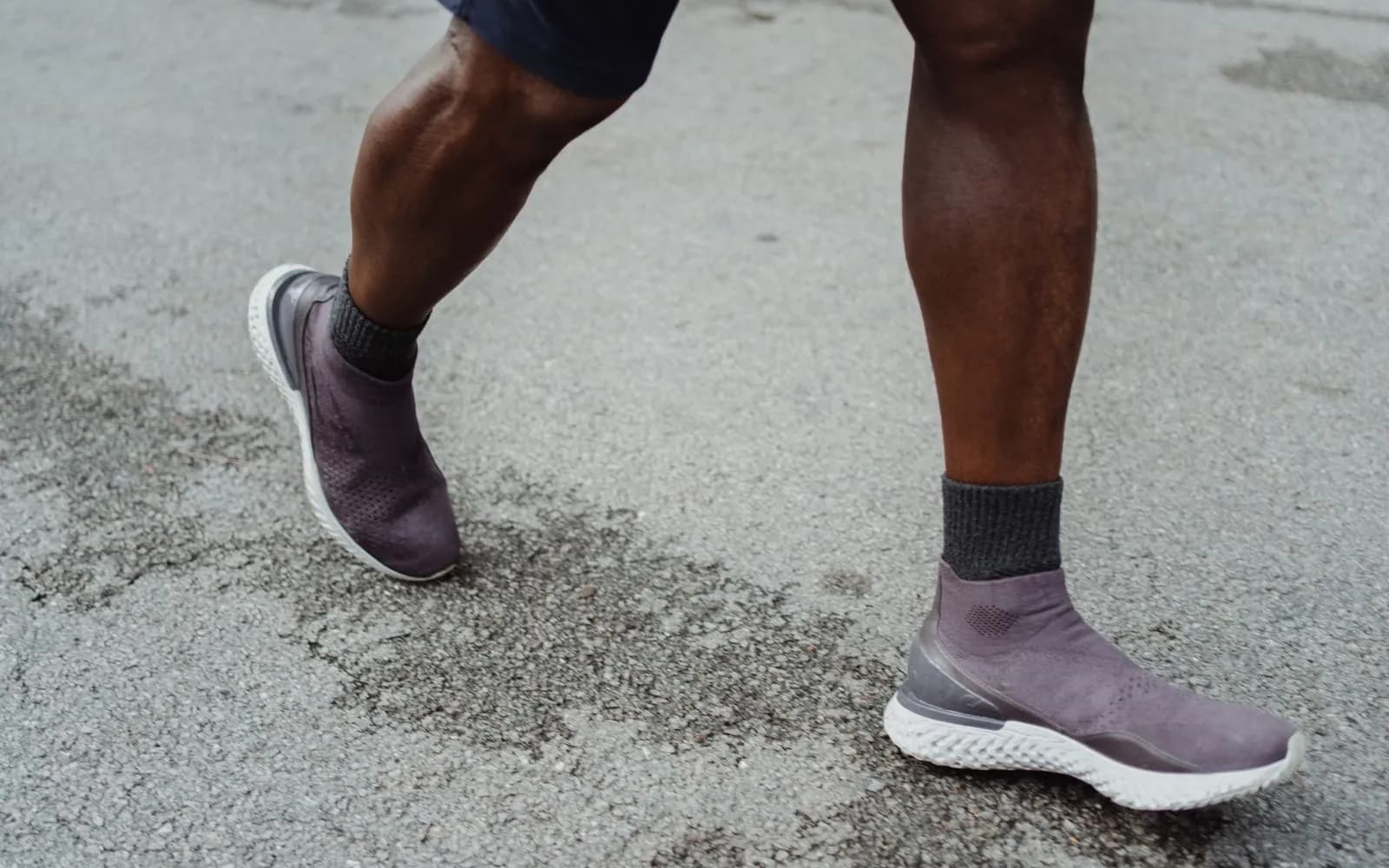 Lower legs of a person in shorts and trainers walking briskly on a tarmac road.