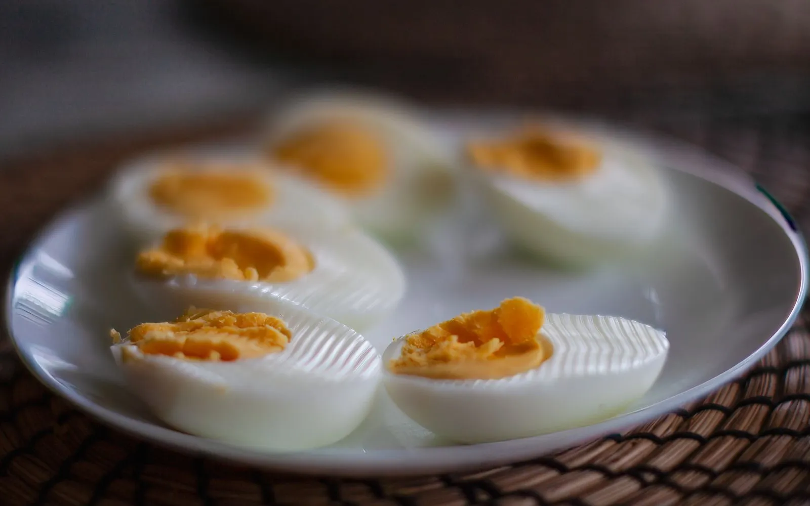 Halved hard-boiled eggs on a white plate on a woven mat
