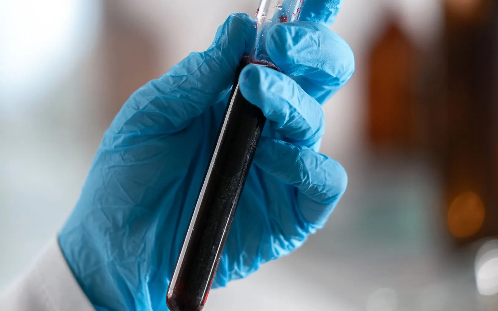 A gloved hand holding a capped test tube of blood in a laboratory