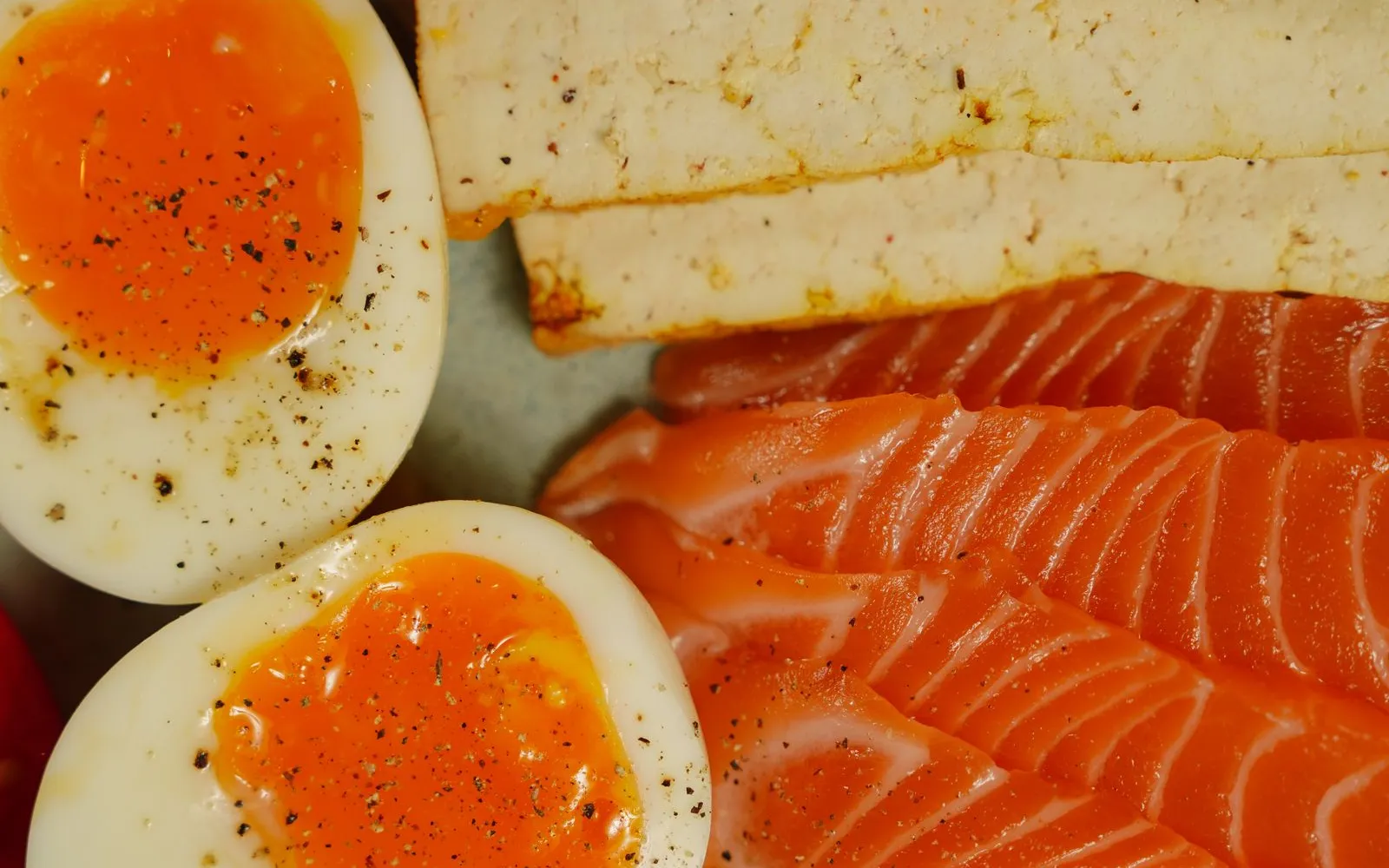 Halved soft-boiled eggs, sliced tofu and slices of salmon with salad leaves on a plate