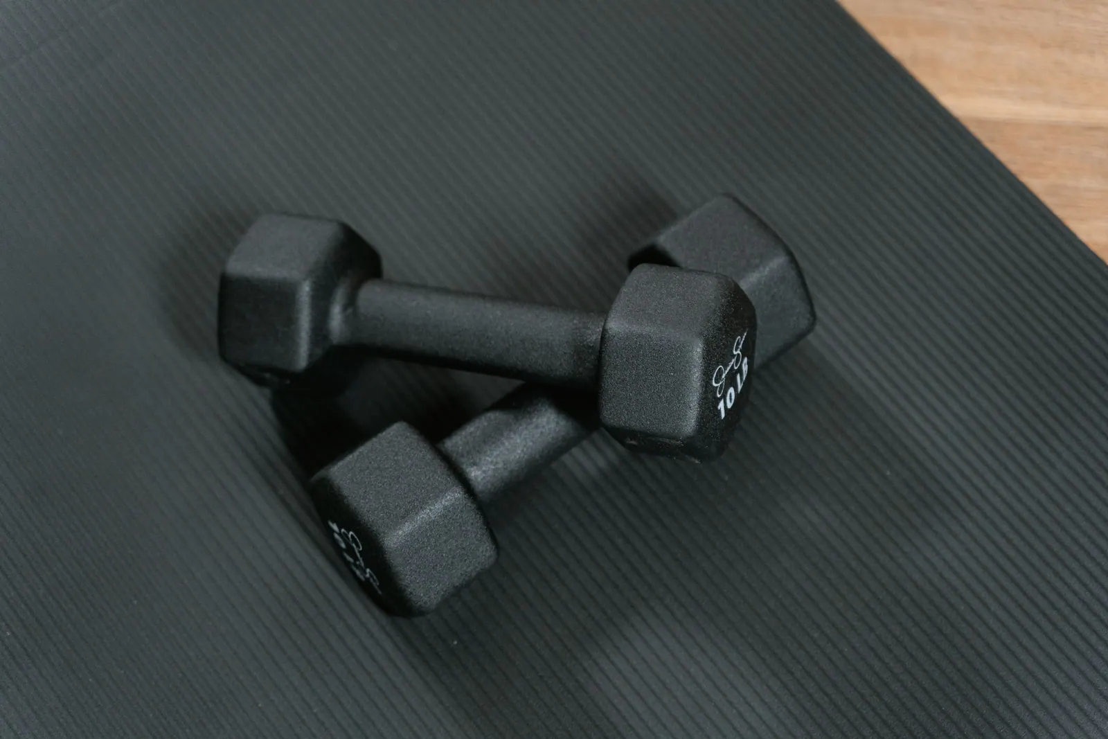 Two dumbbells resting on a dark exercise mat.