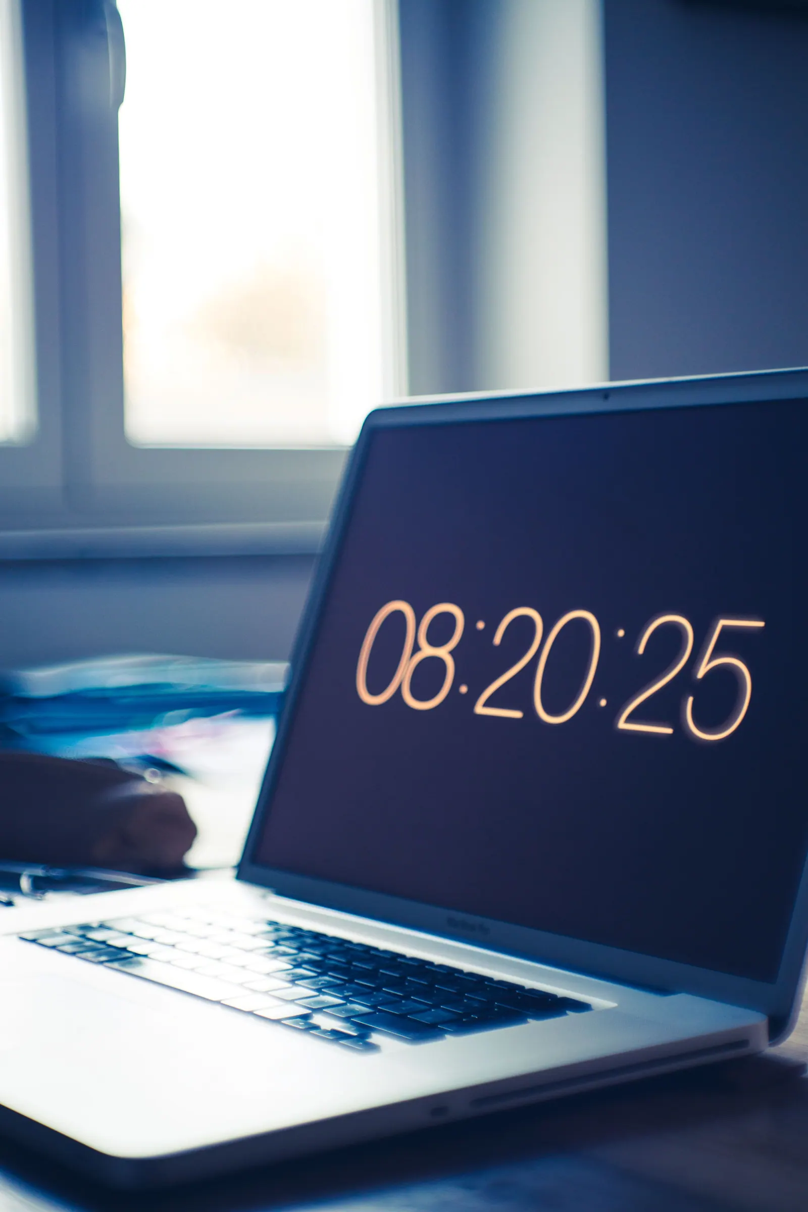 A laptop displaying a clock on a work desk.